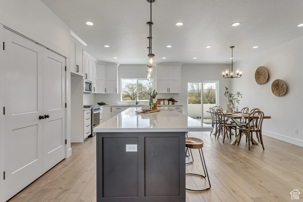 Kitchen with white cabinets, hanging light fixtures, light hardwood / wood-style floors, and stainless steel appliances