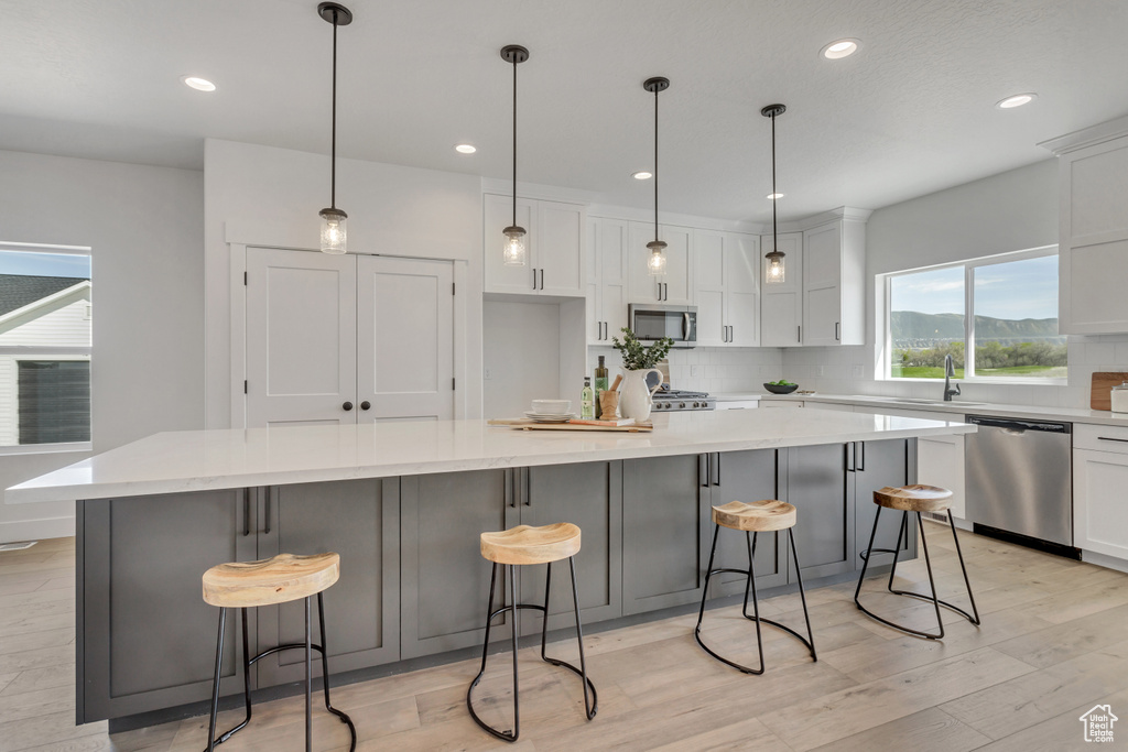 Kitchen with hanging light fixtures, appliances with stainless steel finishes, tasteful backsplash, and a spacious island
