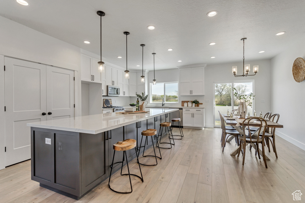 Kitchen with pendant lighting, light hardwood / wood-style flooring, white cabinets, and a spacious island