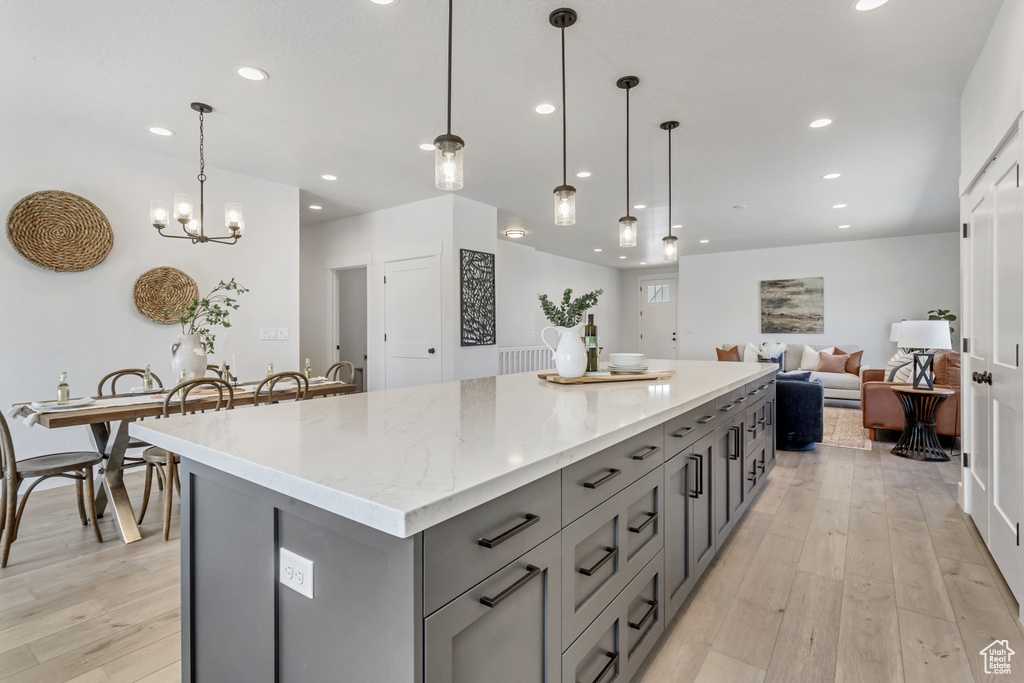 Kitchen with a center island, pendant lighting, light stone countertops, gray cabinetry, and light hardwood / wood-style floors