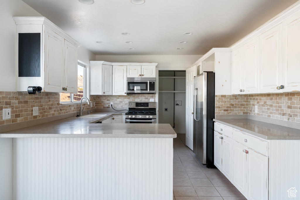 Kitchen featuring white cabinets, light tile flooring, backsplash, appliances with stainless steel finishes, and sink