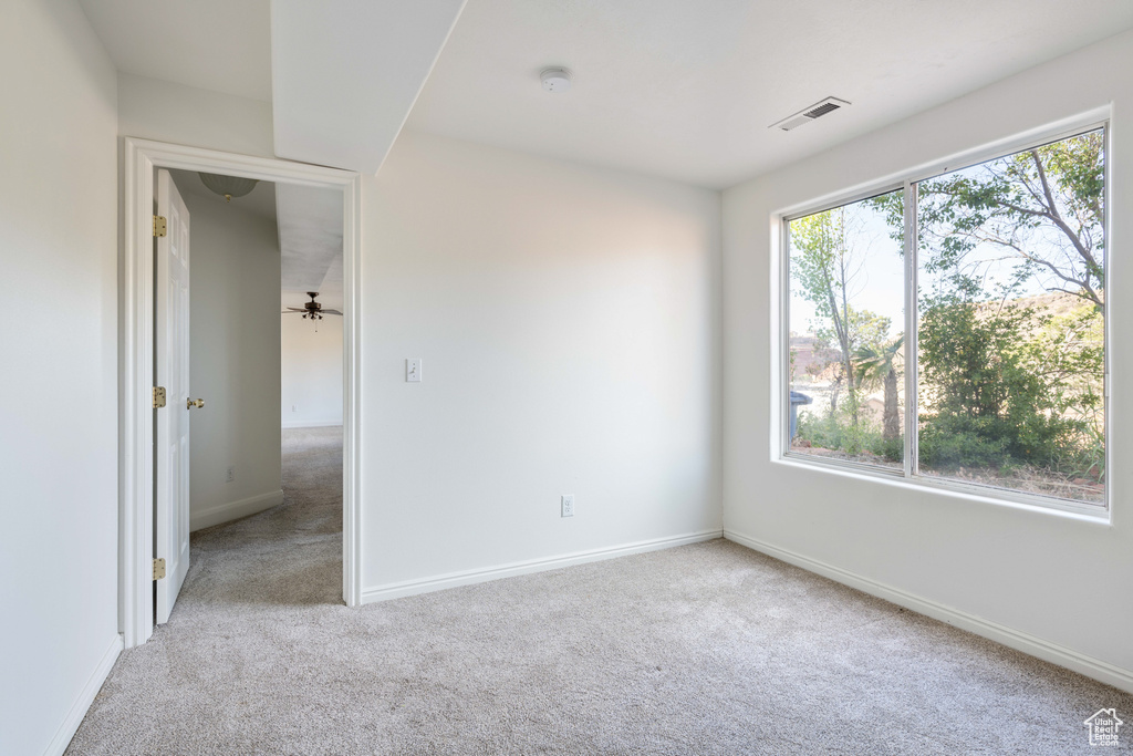 Unfurnished room featuring light carpet, plenty of natural light, and ceiling fan