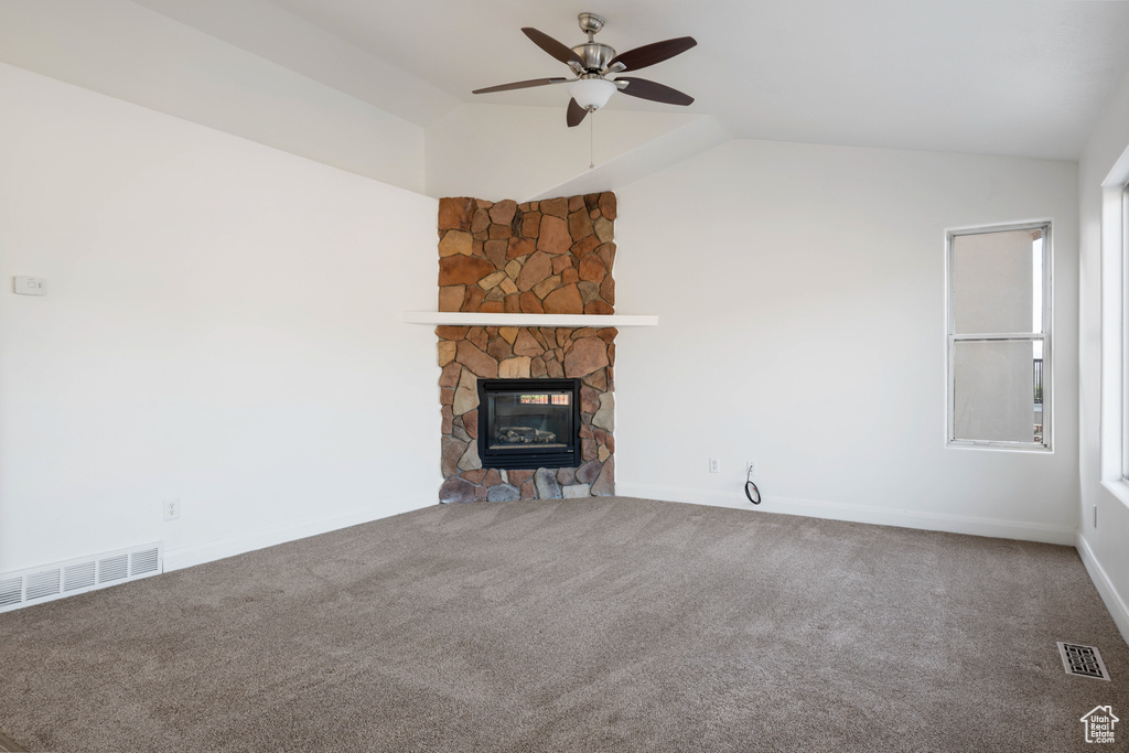 Unfurnished living room featuring ceiling fan, carpet, a stone fireplace, vaulted ceiling, and a healthy amount of sunlight