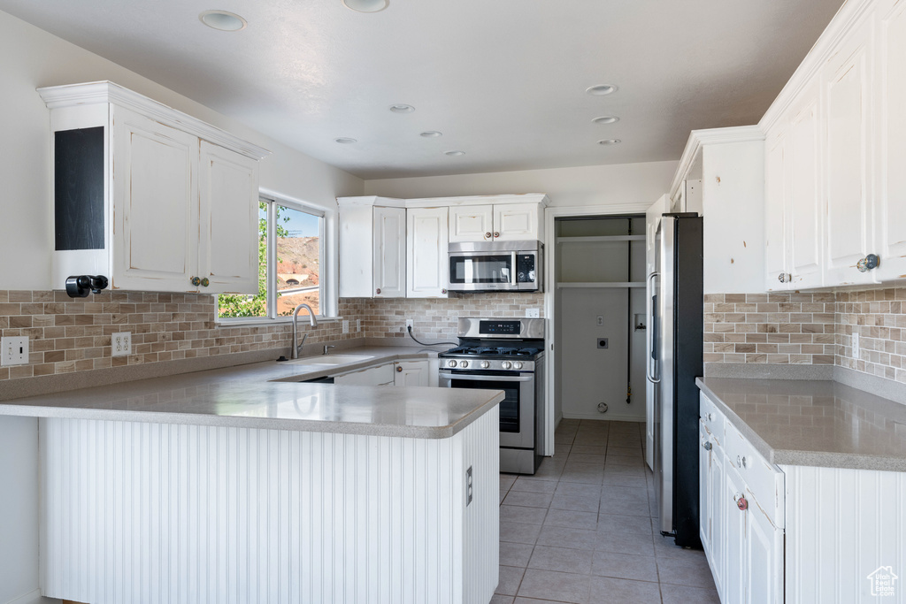 Kitchen featuring white cabinetry, backsplash, appliances with stainless steel finishes, light tile floors, and sink