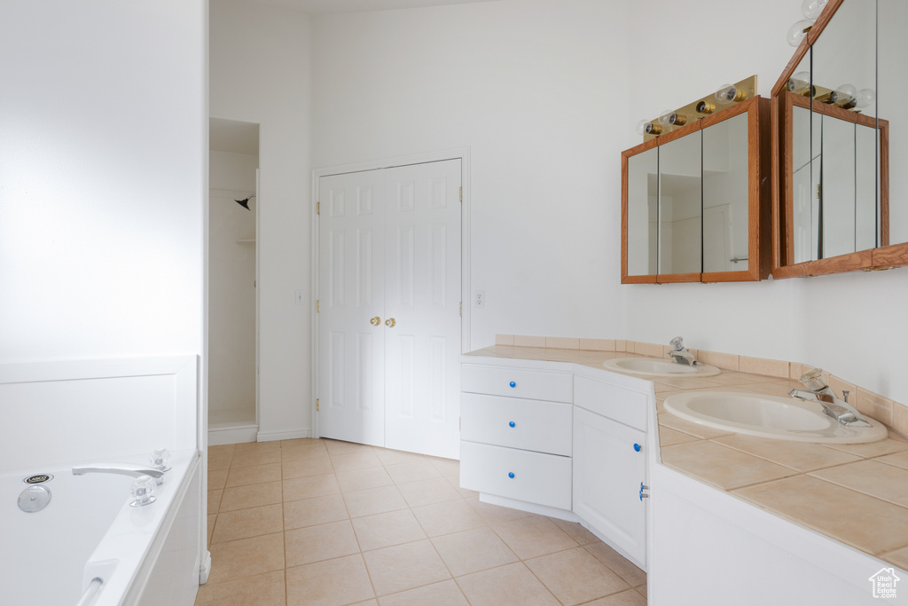 Bathroom featuring a bathing tub, vanity with extensive cabinet space, tile floors, and double sink