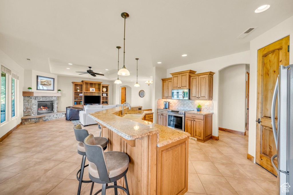 Kitchen with ceiling fan, stainless steel appliances, a spacious island, a fireplace, and light tile floors