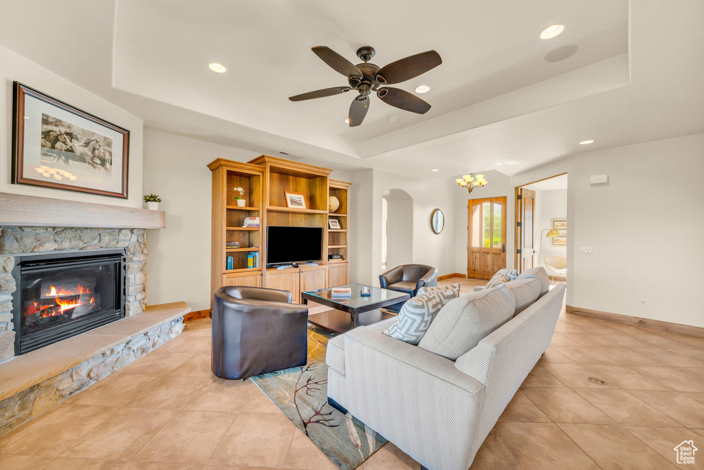Tiled living room featuring a fireplace, a raised ceiling, and ceiling fan