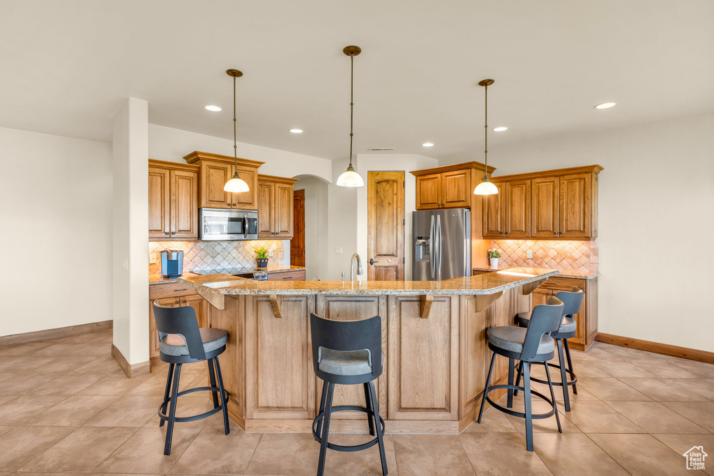 Kitchen featuring hanging light fixtures, stainless steel appliances, backsplash, and light tile floors