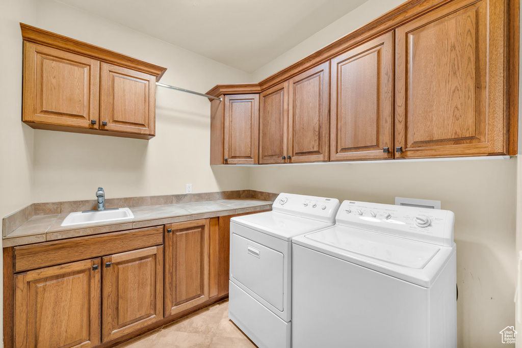 Washroom with sink, cabinets, light tile floors, and washing machine and clothes dryer