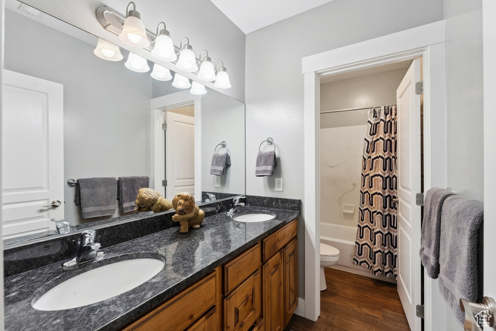 Full bathroom with hardwood / wood-style floors, shower / bath combination with curtain, toilet, and double sink vanity