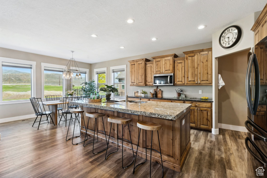 Kitchen featuring dark stone countertops, plenty of natural light, a kitchen island with sink, and dark wood-type flooring