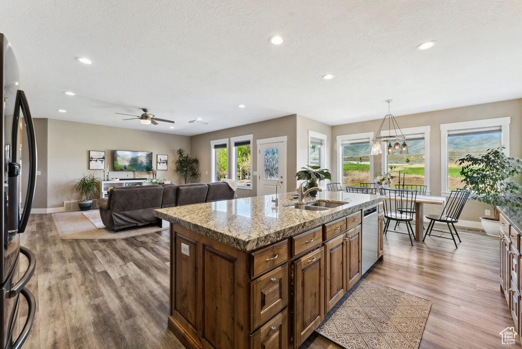 Kitchen with ceiling fan with notable chandelier, a center island with sink, hardwood / wood-style flooring, sink, and pendant lighting