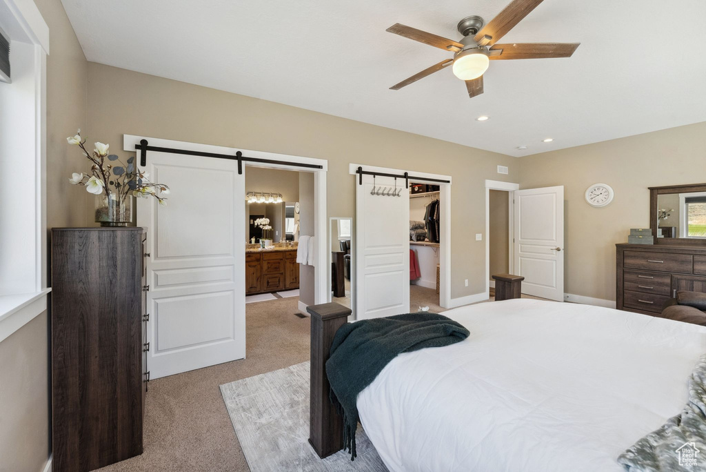 Carpeted bedroom with ceiling fan, a closet, ensuite bath, a barn door, and a walk in closet