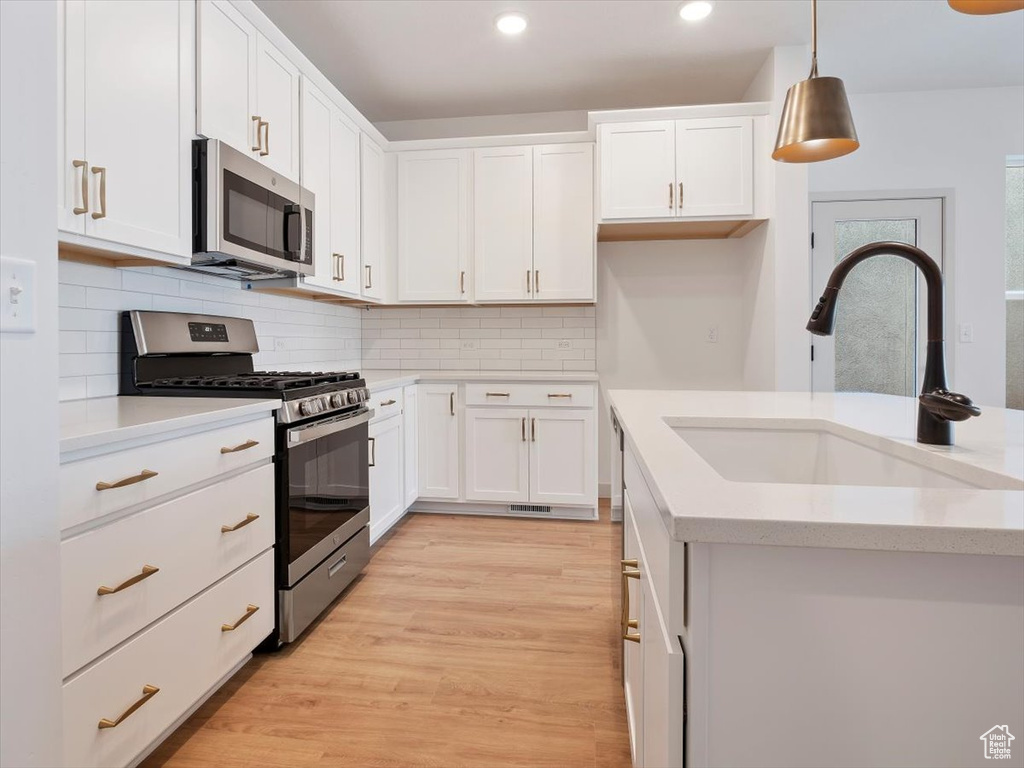 Kitchen featuring white cabinets, sink, light hardwood / wood-style floors, hanging light fixtures, and stainless steel appliances
