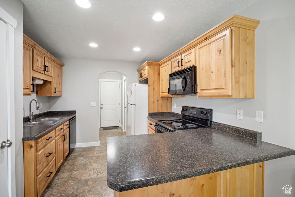 Kitchen with light brown cabinets, kitchen peninsula, black appliances, dark tile flooring, and sink