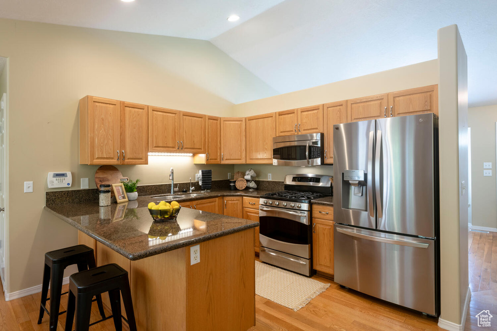 Kitchen featuring kitchen peninsula, stainless steel appliances, sink, light wood-type flooring, and a breakfast bar