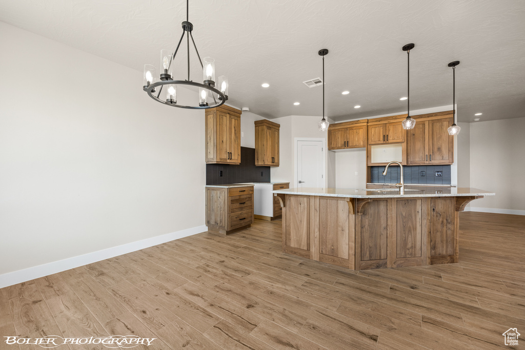 Kitchen featuring light hardwood / wood-style flooring, tasteful backsplash, an island with sink, and decorative light fixtures