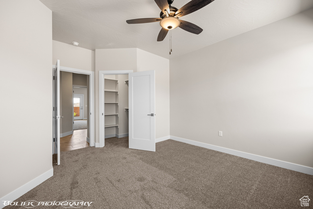 Unfurnished bedroom with a closet, a walk in closet, ceiling fan, and carpet floors