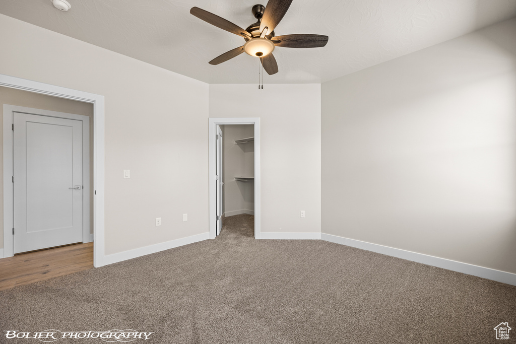 Unfurnished bedroom featuring a closet, a walk in closet, ceiling fan, and carpet floors