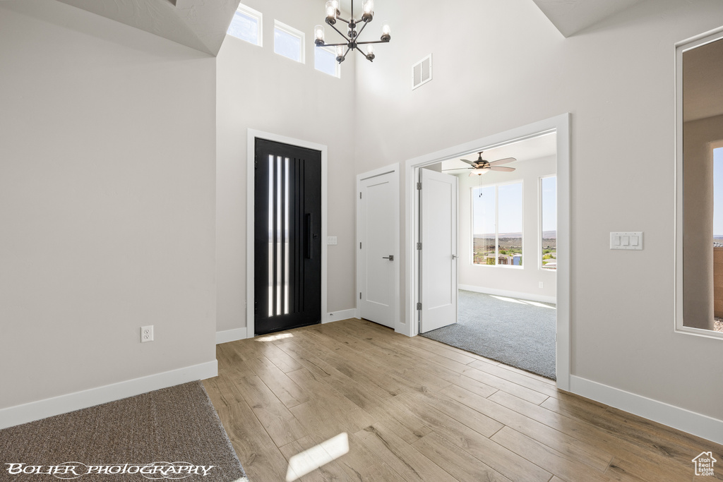 Entryway with ceiling fan with notable chandelier, a towering ceiling, and light hardwood / wood-style floors