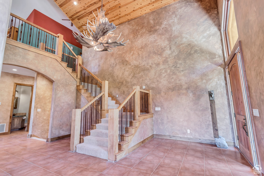 Staircase featuring high vaulted ceiling, tile flooring, a chandelier, and wood ceiling