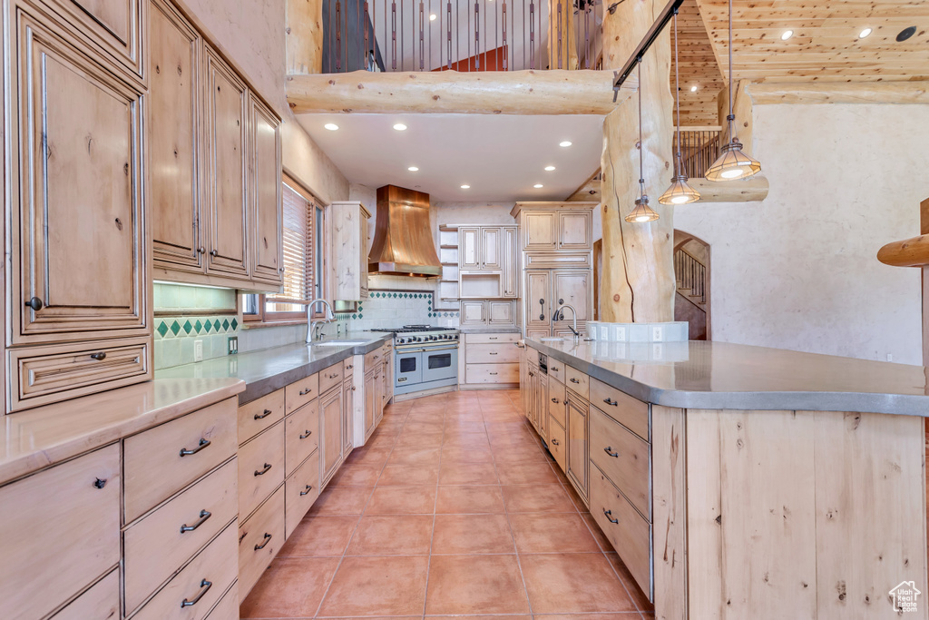 Kitchen with decorative light fixtures, premium range hood, backsplash, double oven range, and light tile floors
