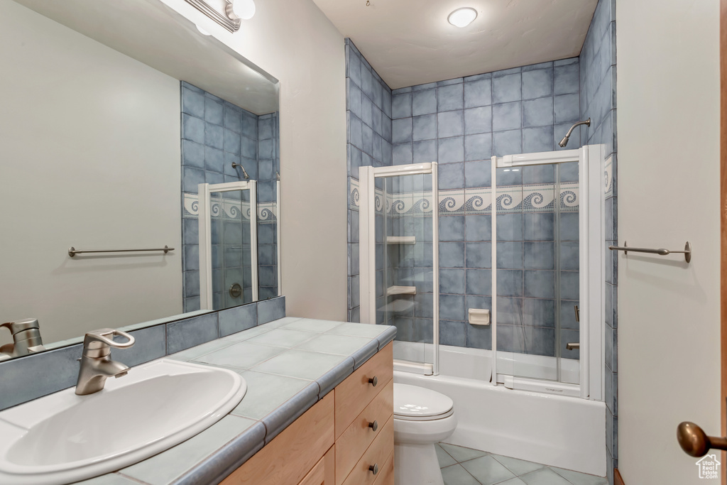 Full bathroom with large vanity, combined bath / shower with glass door, tile floors, and toilet