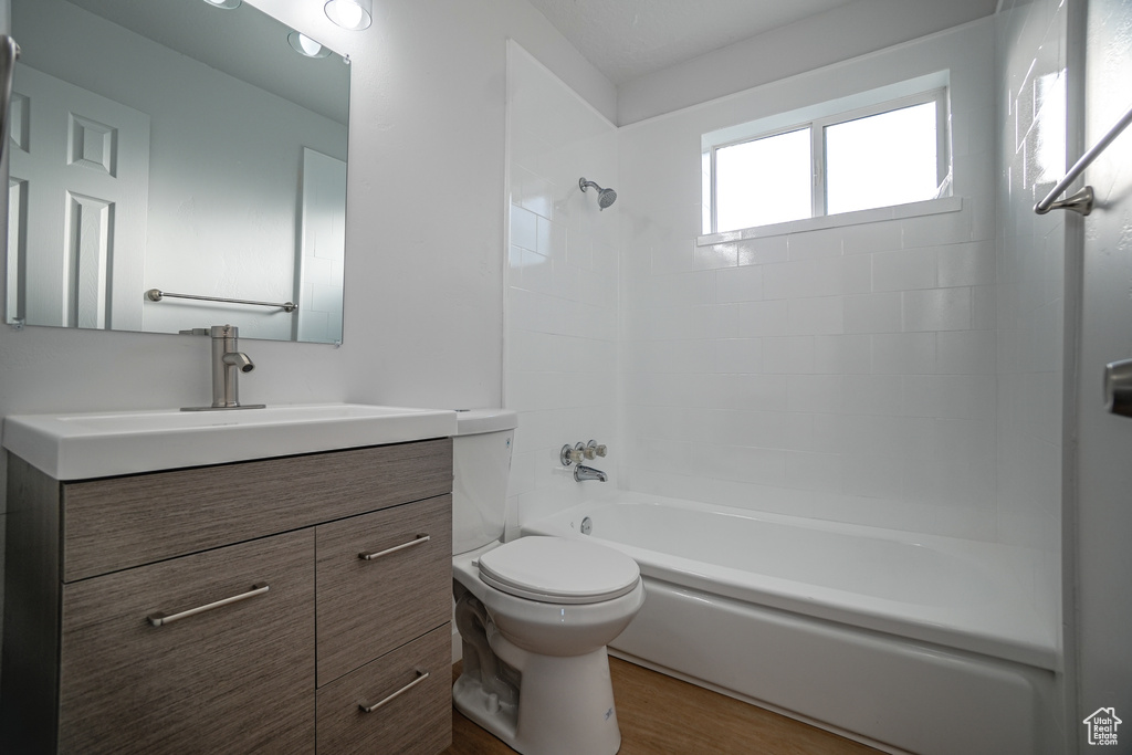 Full bathroom with toilet, tiled shower / bath combo, hardwood / wood-style floors, and large vanity