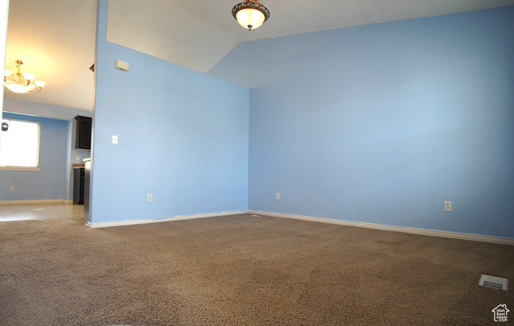 Empty room featuring an inviting chandelier, carpet floors, and lofted ceiling