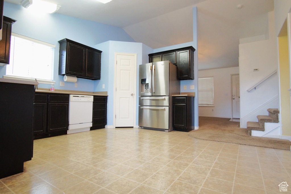 Kitchen with dark brown cabinets, dishwasher, stainless steel fridge, and light tile floors