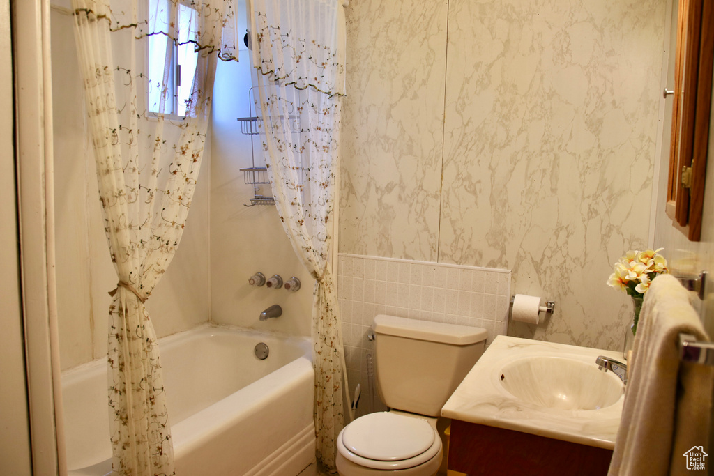 Full bathroom featuring vanity, shower / bath combo with shower curtain, toilet, and tile walls