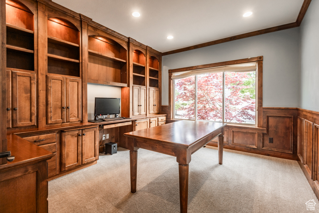 Home office featuring light carpet, crown molding, and built in desk