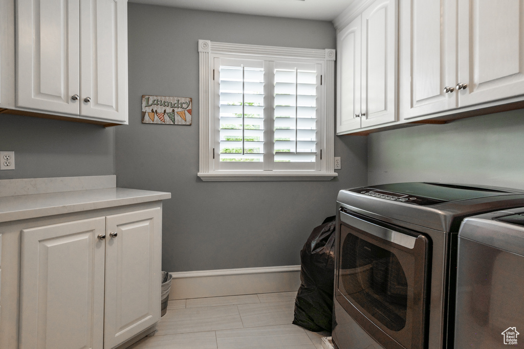 Laundry area with washing machine and clothes dryer, cabinets, and light tile floors