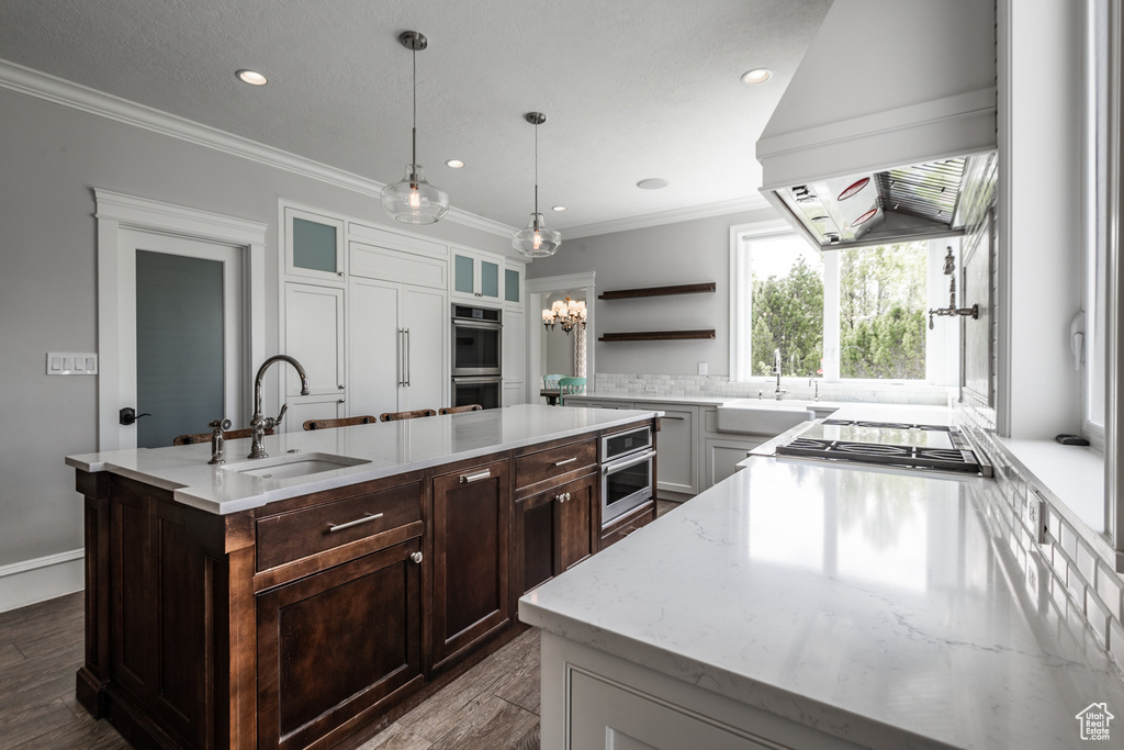 Kitchen featuring light stone counters, a kitchen island with sink, sink, premium range hood, and pendant lighting