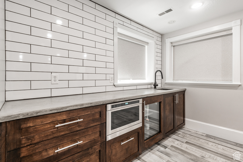 Kitchen featuring oven, dark brown cabinets, sink, tasteful backsplash, and light hardwood / wood-style floors