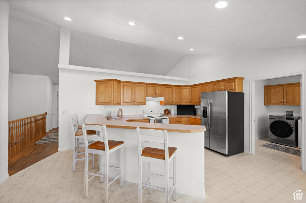Kitchen with high vaulted ceiling, stainless steel fridge with ice dispenser, electric stove, washer / clothes dryer, and light tile floors
