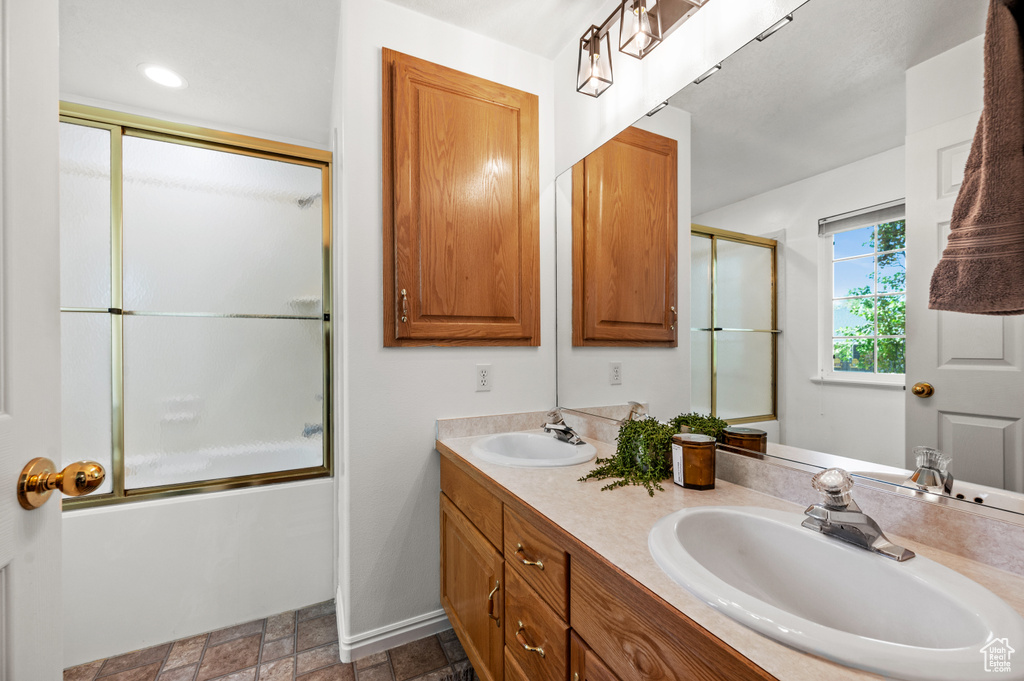 Bathroom with combined bath / shower with glass door, vanity with extensive cabinet space, and double sink