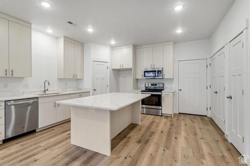 Kitchen with a kitchen island, stainless steel appliances, white cabinetry, sink, and light wood-type flooring