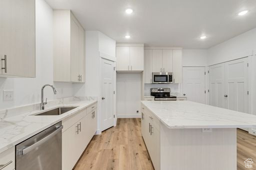 Kitchen with light hardwood / wood-style flooring, stainless steel appliances, white cabinets, sink, and a center island