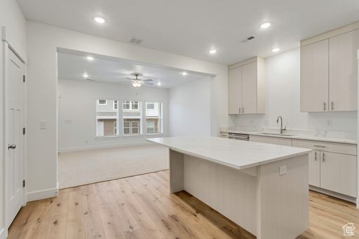 Kitchen with light carpet, white cabinetry, sink, a kitchen island, and ceiling fan