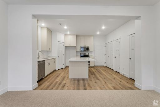 Kitchen featuring a center island, light carpet, sink, white cabinetry, and stainless steel appliances