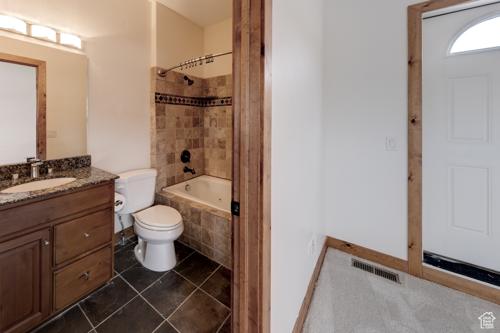 Full bathroom with tiled shower / bath combo, large vanity, toilet, and tile flooring