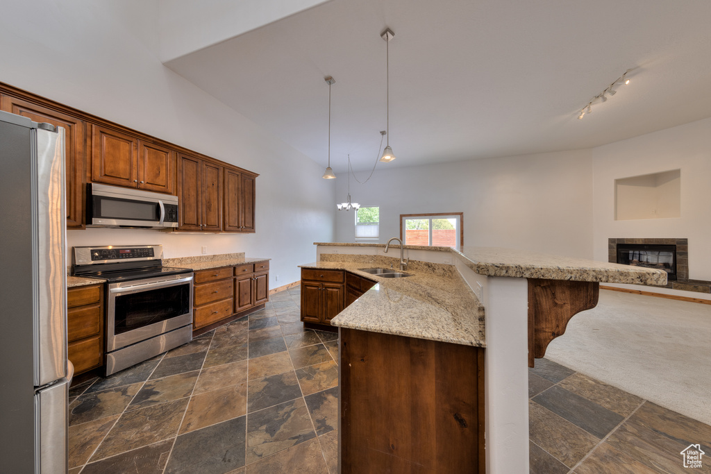 Kitchen featuring hanging light fixtures, stainless steel appliances, a center island with sink, a tile fireplace, and sink