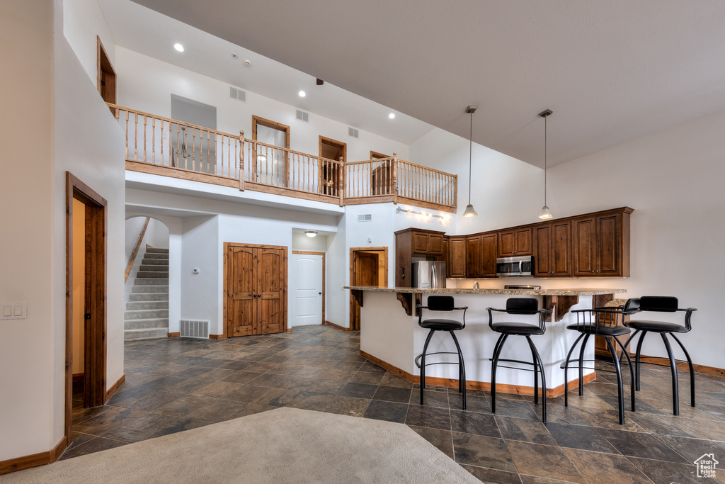 Kitchen featuring appliances with stainless steel finishes, dark tile floors, a towering ceiling, a kitchen bar, and decorative light fixtures