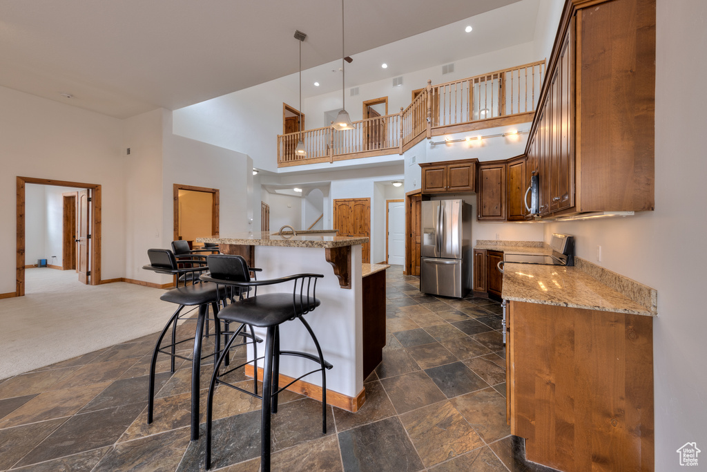 Kitchen with a towering ceiling, light stone countertops, hanging light fixtures, stainless steel appliances, and dark tile flooring