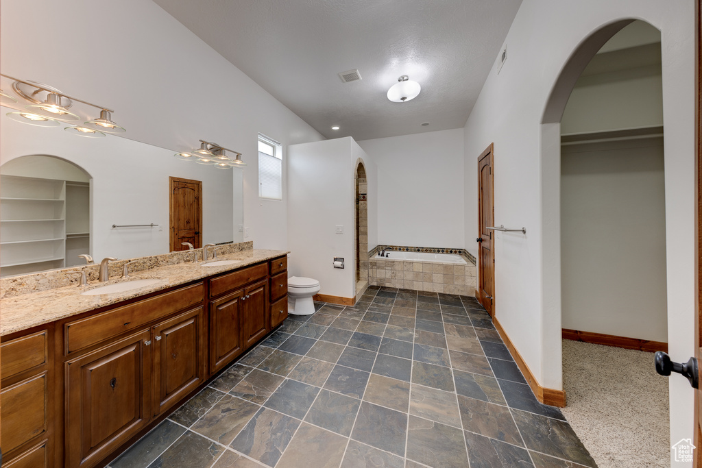 Bathroom with a bathtub, dual bowl vanity, toilet, and tile flooring