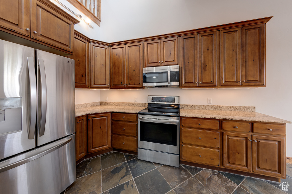Kitchen with appliances with stainless steel finishes, dark tile flooring, and light stone countertops
