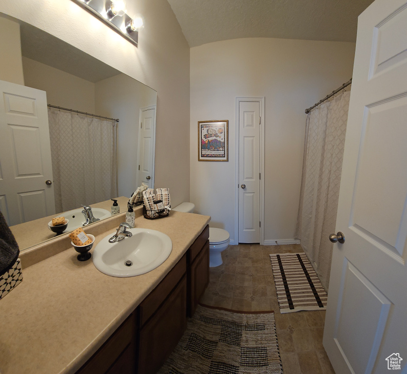 Bathroom with toilet, tile flooring, vanity, and lofted ceiling