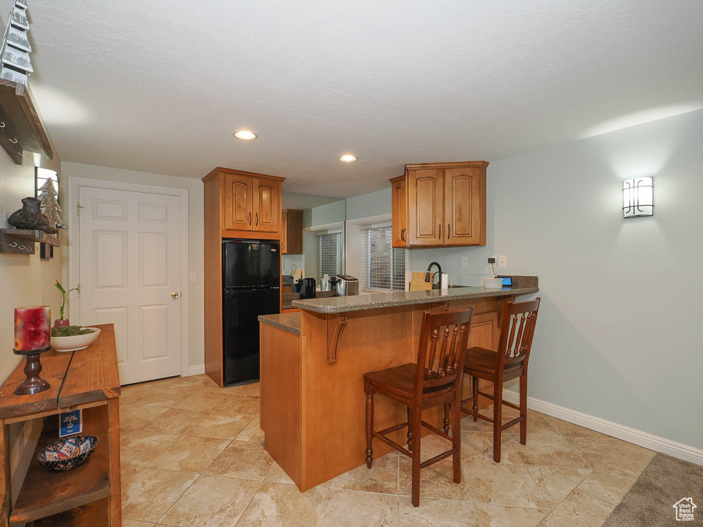 Kitchen featuring light tile floors, sink, a breakfast bar area, black refrigerator, and kitchen peninsula