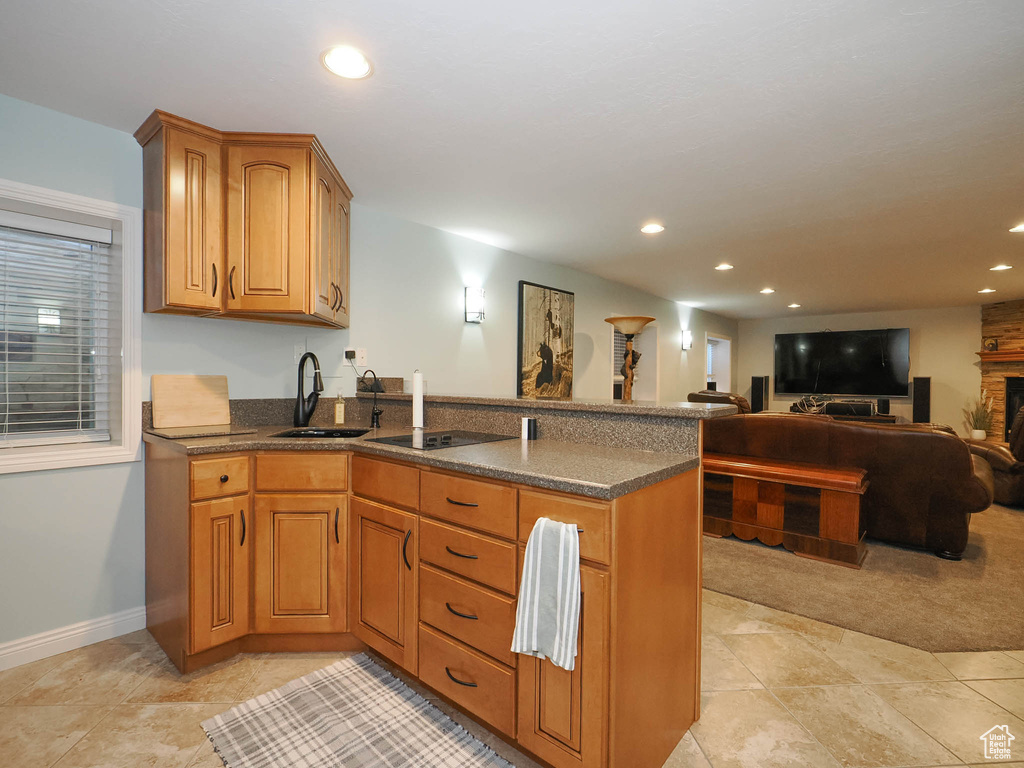 Kitchen with dark stone countertops, sink, light carpet, and kitchen peninsula